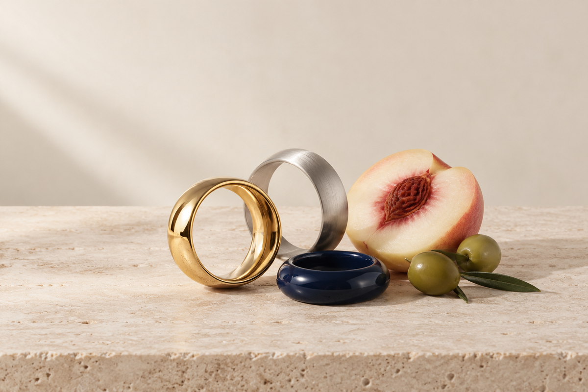 Abstract gold, brushed silver and navy ring forms styled with a peach and green olives on warm limestone.