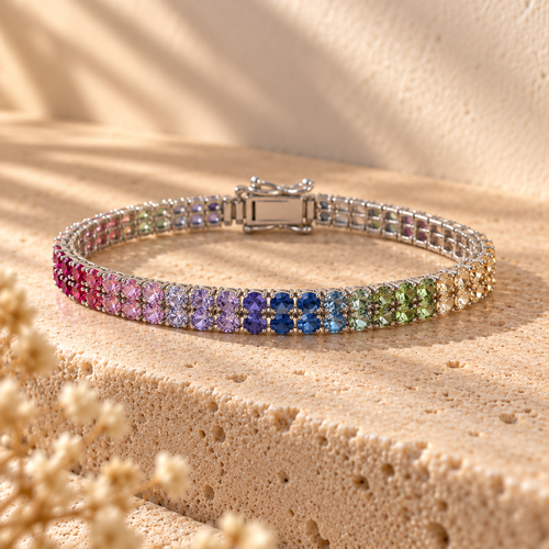 Color Theory rainbow double-row tennis bracelet on a travertine ledge