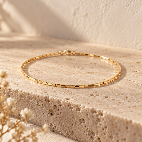 Thin Margin flat-link gold bracelet on a travertine ledge