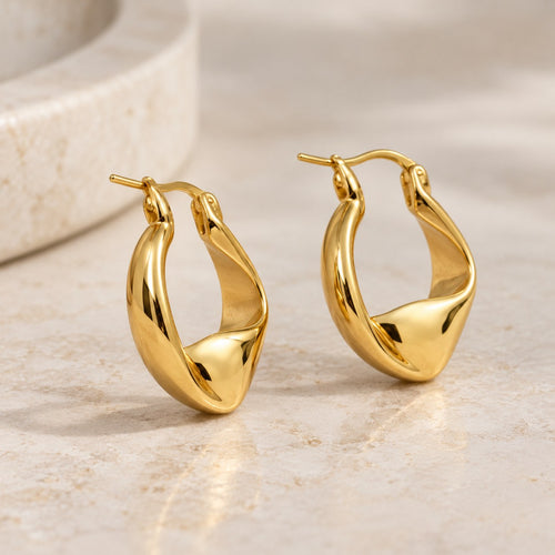 Plot Twist twisted gold hoop earrings styled on a travertine ledge