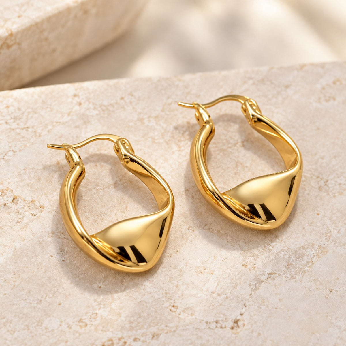 Plot Twist twisted gold hoop earrings on warm stone