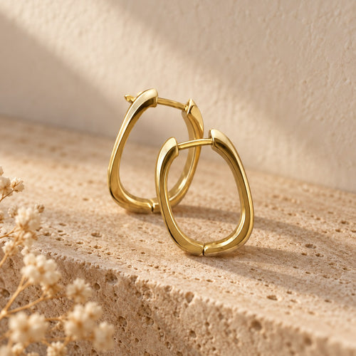 Square Deal squared hoop earrings in gold on a travertine ledge