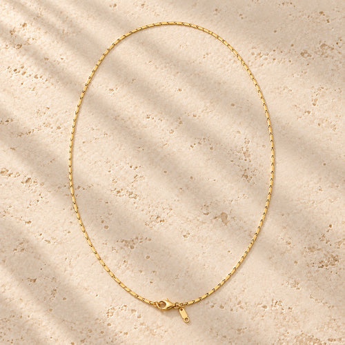 Thin Margin necklace laid in a full loop on travertine