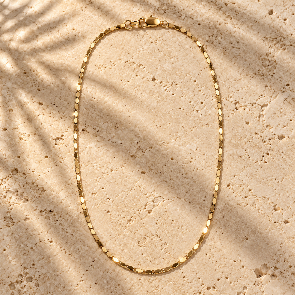 Bar None gold cobra chain necklace on travertine, flat polished plates catching the light