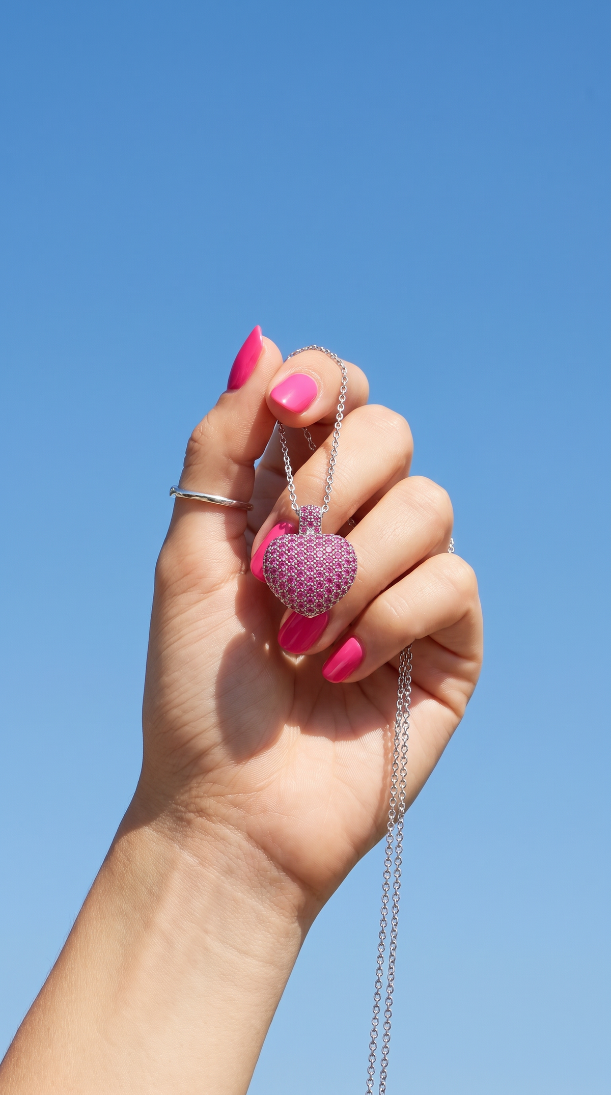 Be Still My Heart pink pavé heart pendant held against a blue sky