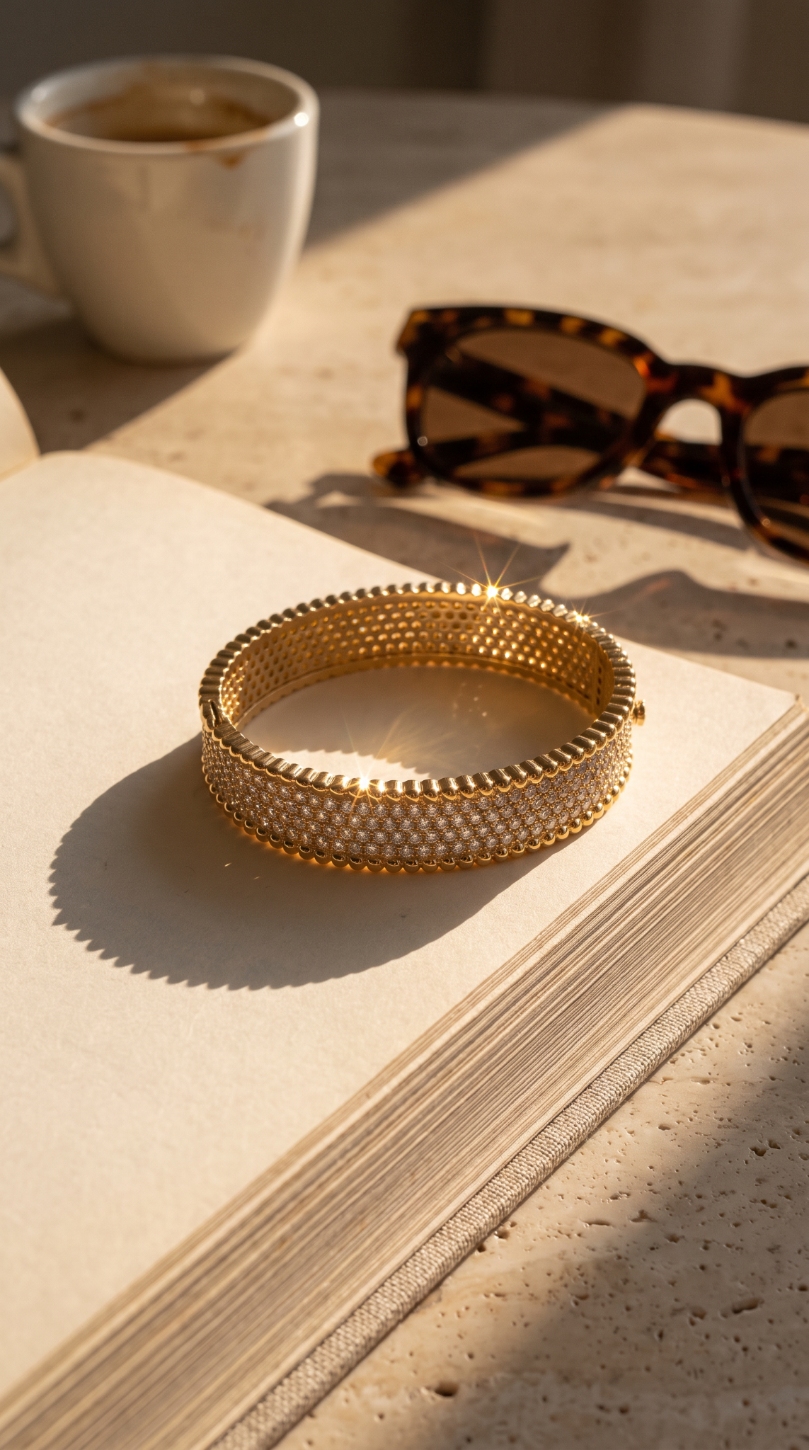 Pavé the Way gold pavé bracelet styled on a book beside sunglasses and coffee