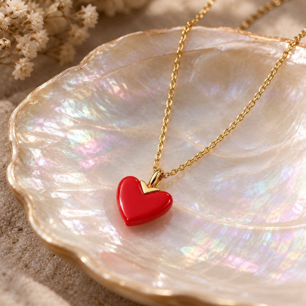 Red Letter Day red enamel heart pendant with gold V-cap on a gold chain, on a shell dish