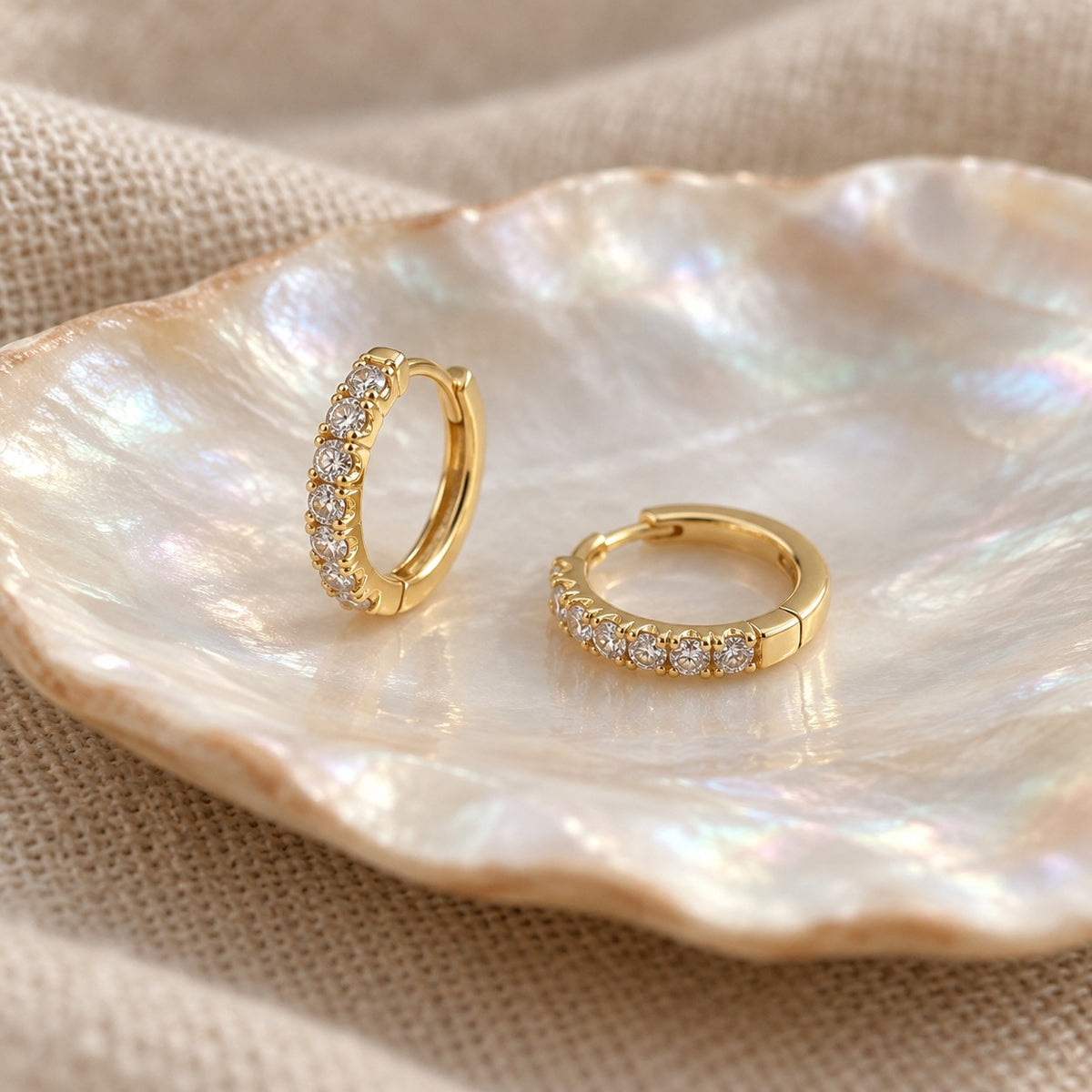 Small Talk gold huggie hoop earrings with a row of rhinestones on an iridescent shell dish (BU-ER-007)