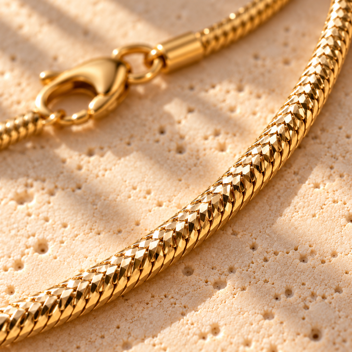 Bar None diamond-cut snake chain macro close-up: faceted gold scales catching the light, with the lobster clasp
